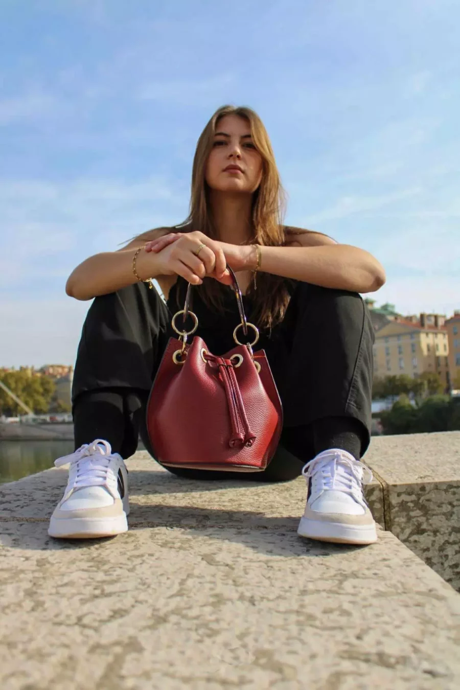 Ce sac bourse bordeaux de confection italienne est équipé d'une bandoulière en chaîne dorée garnie de cuir, à la fois réglable et amovible, ainsi qu'une large poignée. Vous pourrez le porter aussi bien à la main qu'en bandoulière, avec confort et style. Pratique et spacieux, le sac bourse dispose d'un intérieur bien organisé avec une poche simple, et se ferme aisément à l'aide d'un lien de serrage. Il est sublimé par des pièces métalliques dorées | Dovelya